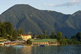 Tegernsee with sailing boats and boat huts, warm evening light, town Tegernsee, mountain Wallberg,