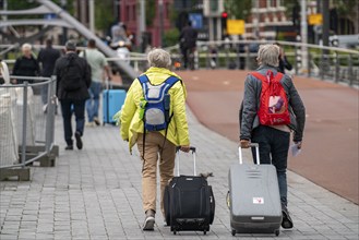 Travellers on their way to a river cruise ship at the quay of the Ij, transporting their luggage,