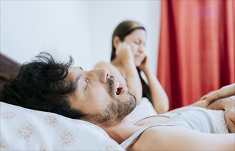 Snoring man in bedroom and wife covering her ears. Husband snoring while the wife suffers and