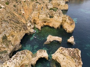 Rocky cliffs and cave formations in clear blue water with a small boat, aerial view, Ponta da