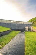 A river flowing under a large concrete dam, surrounded by grass and nature, Rappbode Dam, Harz