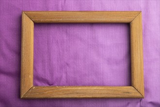 Wooden frame on smooth cotton purple tissue. Top view, flat lay, natural textile background and