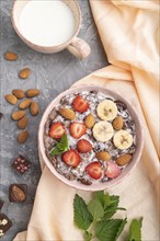 Chocolate cornflakes with milk, strawberry and almonds in ceramic bowl on gray concrete background