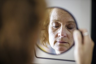 Symbol photo. An elderly woman with closed eyes can be seen in a mirror. Berlin, 13.08.2024