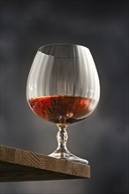 Facetted glass with brandy, quarter-filled with amber cognac stands on a rustic wooden shelf