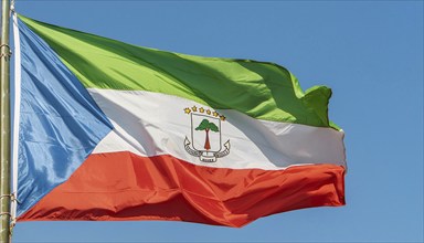 The flag of Equatorial Guinea flutters in the wind, isolated against a blue sky