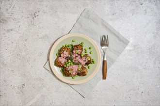 Top view of meatballs with fresh green peas and cranberry sauce on grey stone background