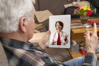 Symbolic image of telemedicine, elderly patient speaking to a doctor in a video conference from