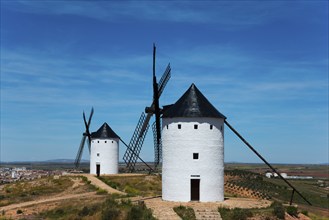 Two white windmills on a hill overlooking a vast landscape under a blue sky on a sunny day, Alcazar