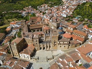 Aerial view of an old monastery with red roofs, surrounded by a village and green hills, presenting