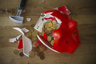 Symbolic photo on the subject of saving. An open, broken piggy bank with coins and banknotes stands