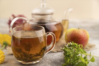 Red tea with herbs in glass teapot on brown concrete background and linen textile. Healthy drink