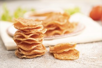 Slices of dehydrated salted meat chips with herbs and spices on gray concrete background and white