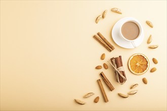 Composition with almonds, cinnamon and cup of coffee on orange pastel background. Blank, flat lay,