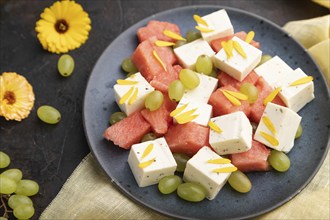 Vegetarian salad with watermelon, feta cheese, and grapes on blue ceramic plate on black concrete