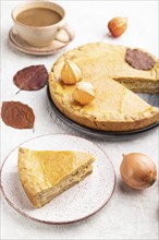 Autumn onion pie decorated with leaves and cup of coffee on gray concrete background. Side view,