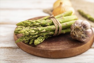 Bunch of fresh green asparagus, garlic, onion on white wooden background. Side view, selective