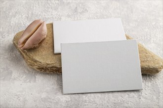 White paper business card, mockup with natural stone and seashell on gray concrete background.