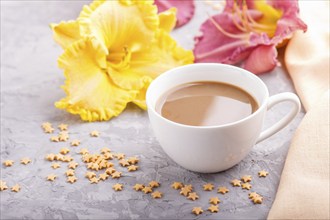 Yellow anf purple day-lilies cup of coffee on a gray concrete background, with orange textile.