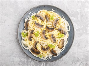 Rice noodles with champignons mushrooms, egg sauce and oregano on blue ceramic plate on a gray