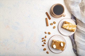 Honey cake with milk cream, caramel, almonds and a cup of coffee on a white concrete background and