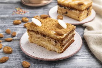 Honey cake with milk cream, caramel, almonds and a cup of coffee on a gray wooden background and