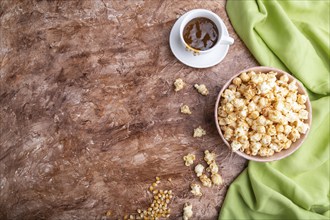 Popcorn with caramel in ceramic bowl on brown concrete background and green textile. Top view, flat