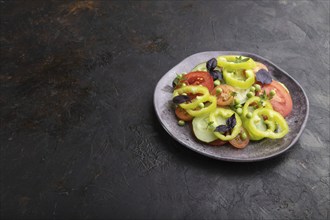 Vegetarian salad from green pea, tomatoes, pepper and basil on a black concrete background. Side