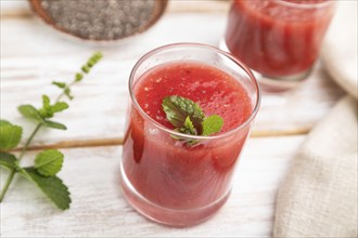 Watermelon juice with chia seeds and mint in glass on a white wooden background with linen textile.