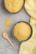 Blue ceramic bowl with raw golden rice and wooden spoon on a gray concrete background and yellow