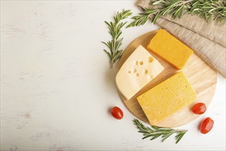 Various types of cheese with rosemary and tomatoes on wooden board on a white wooden background and