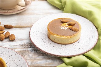 Sweet tartlets with almonds and caramel cream with cup of coffee on a white wooden background and