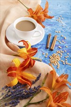 Orange day-lily and lavender flowers and a cup of coffee on a blue concrete background, with orange