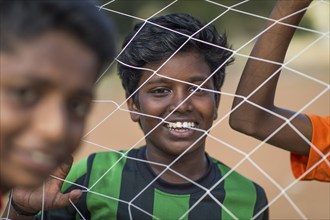 Laughing boys looking through goal net, football, Parade Ground, Fort Cochin, Kochi, Kerala, South