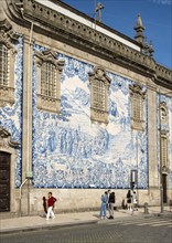 People pass by the facade of Igreja do Carmo church, adorned with intricate blue and white tiles,