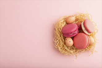 Purple and pink macaroons and chocolate eggs in decorative paper nest on pink pastel background.