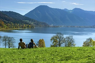 Tegernsee with Wallberg, couple sitting on a green meadow and looking at the lake, trees