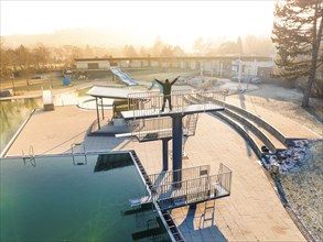 A person stands on a diving platform in a swimming pool at sunrise in winter, ENCW outdoor pool