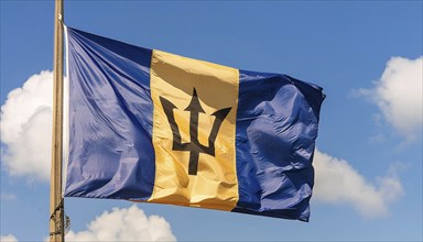 The Barbados flag flutters in the wind, isolated against a blue sky