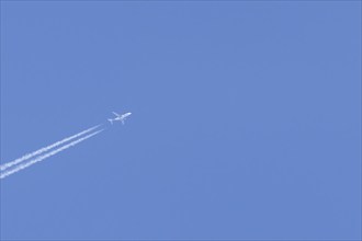 Jet aircraft in flight with a contrail or vapour trail across a blue sky, England, United Kingdom,