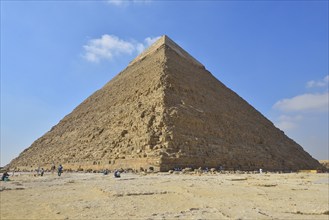 The Great Pyramid of Giza under a clear blue sky with a few scattered clouds, surrounded by