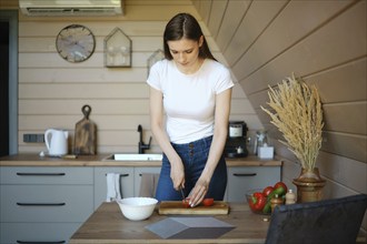 Young woman slicing fresh tomato on wooden chopping board in a wooden kitchen