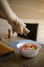 Close-up view of adding sea salt from a hand mill to a bowl with vegetable salad