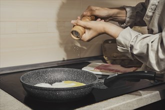 Unrecognizable woman adding salt to eggs in frying pan