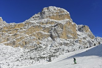 Skiers on the descent from Col Pradat in front of the snow-covered peak of Sassongher, winter