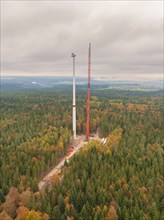 An almost completed wind turbine and a crane in an autumnal forest, wind farm construction site,