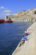 Men fishing historic waterfront buildings on quayside, Valletta, Malta, Europe