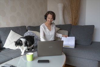 Woman, mid-50s, works from home, with laptop and communicates with colleagues via headset, home