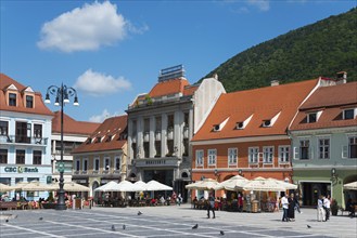 Sunny market square with historical buildings, people at street cafés and mountain in the