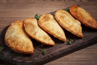 Fried chebureks, deep-fried, mini, on a chopping board, wooden table, close-up, no people